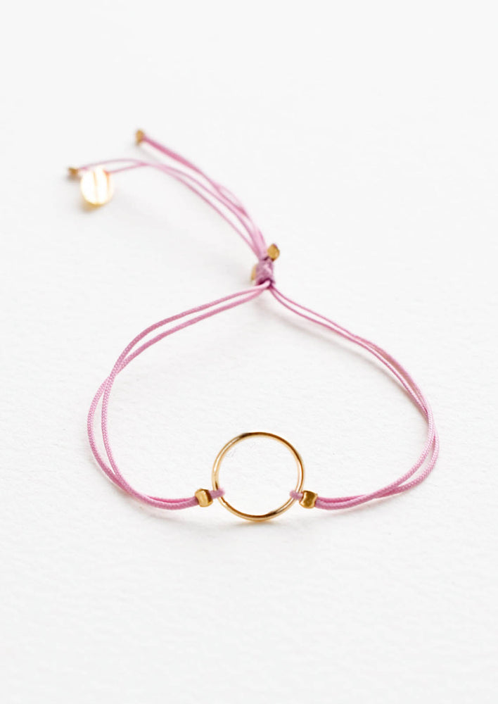 Bracelet with yellow gold circle charm centered on an adjustable purple string.