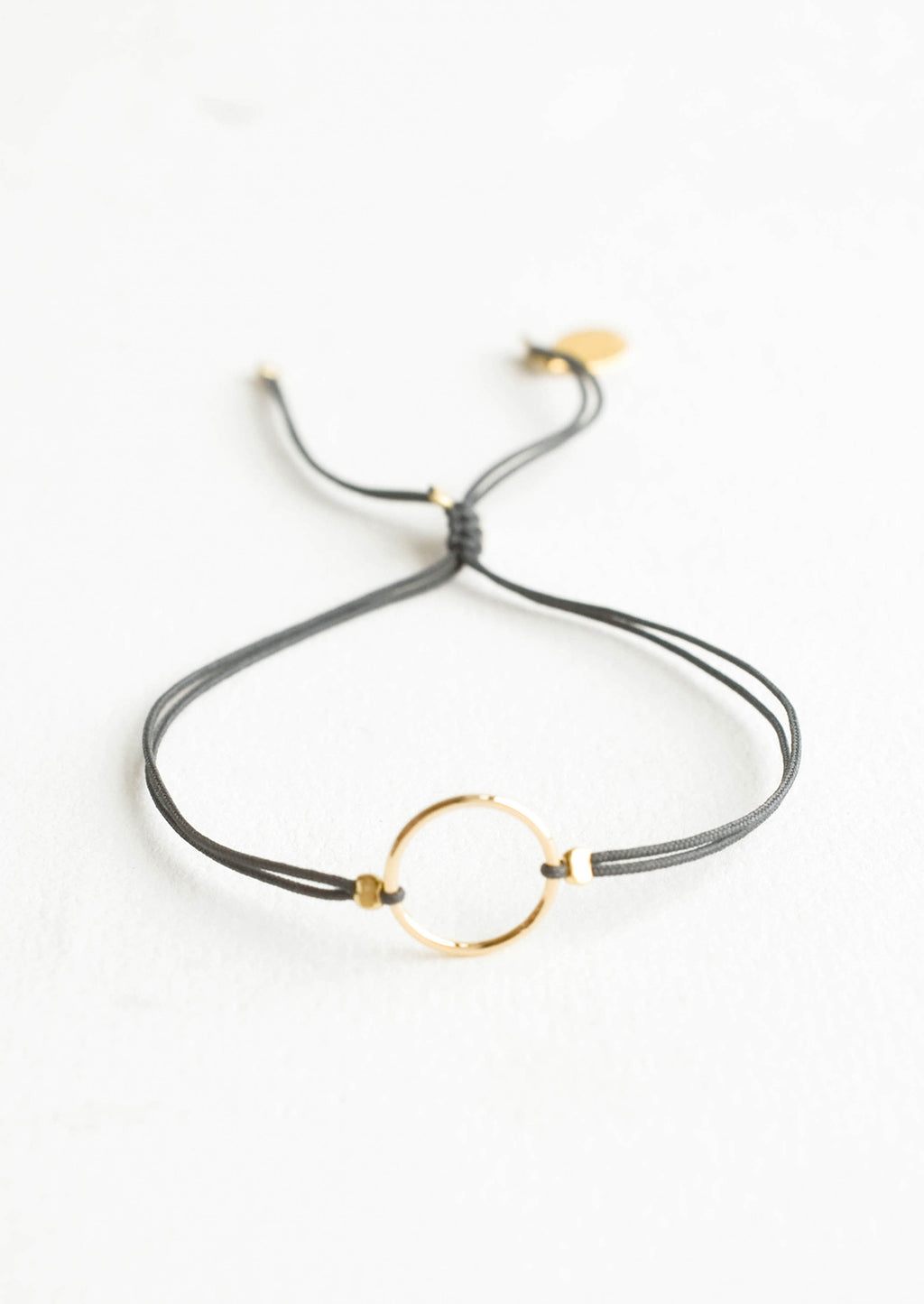Charcoal: Bracelet with yellow gold circle charm centered on an adjustable dark grey string.