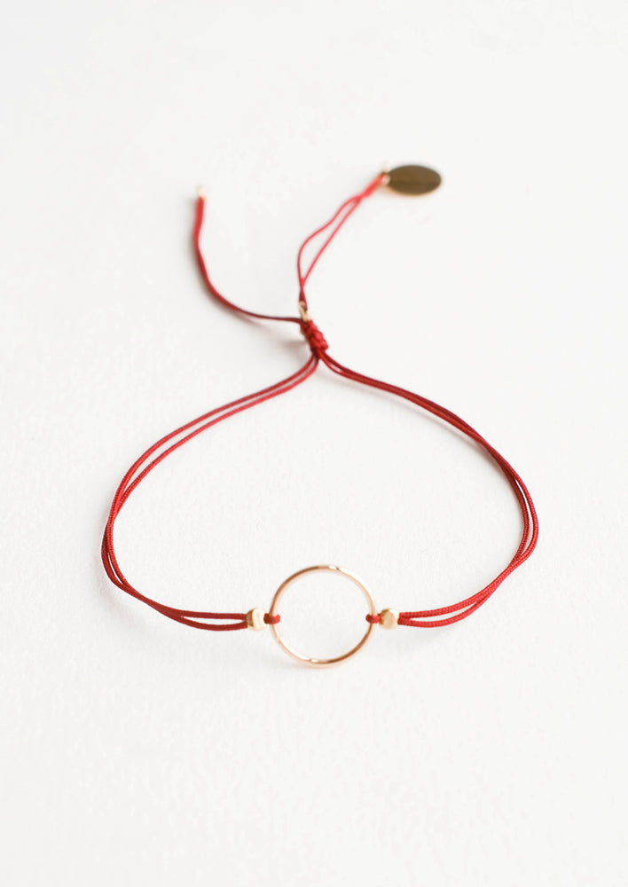 Bracelet with yellow gold circle charm centered on an adjustable dark red string.