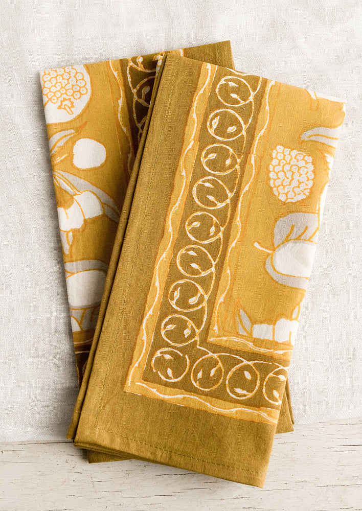 A pair of mustard/gold napkins with fruit print.