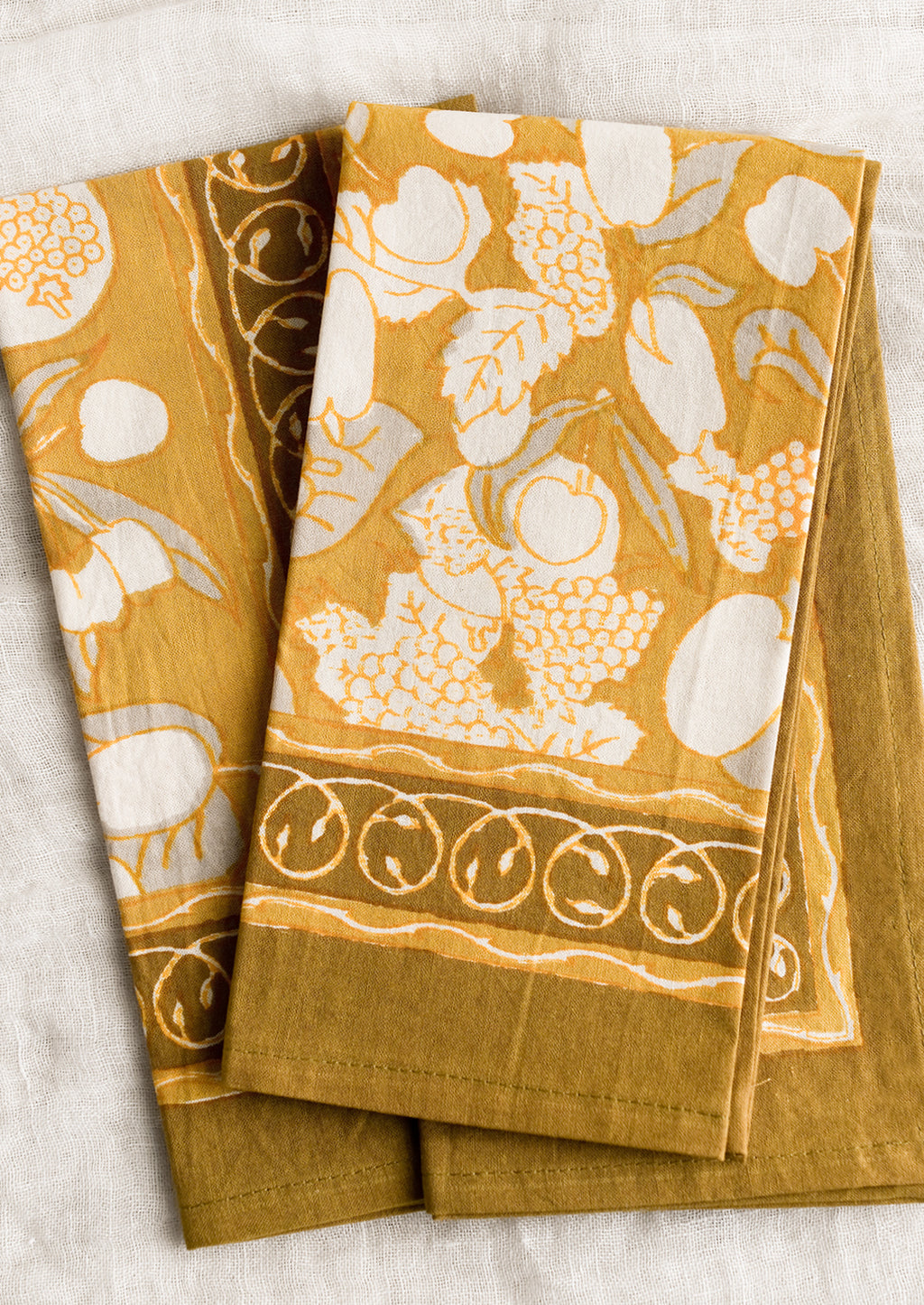 1: A pair of mustard/gold napkins with fruit print.