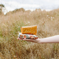 4: Arm extended across meadow holding two beeswax wrapped objects.