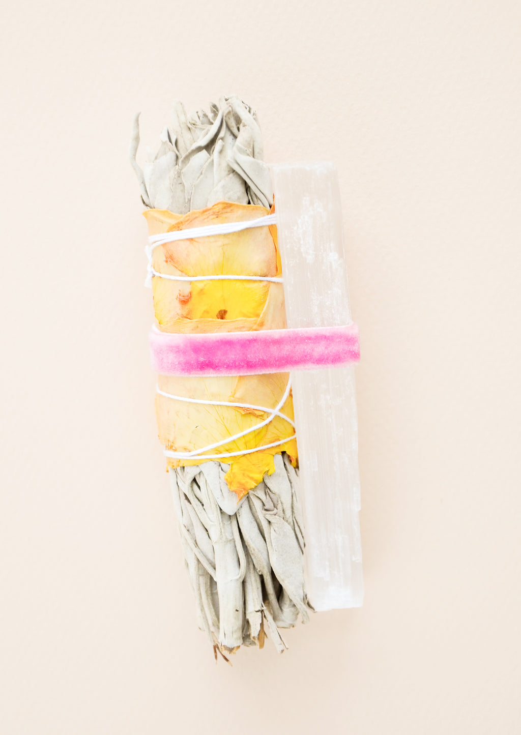 1: A dried sage bundle wrapped in yellow and pink dried rose petals alongside a rectangular white crystal both secured by a pink velvet ribbon.