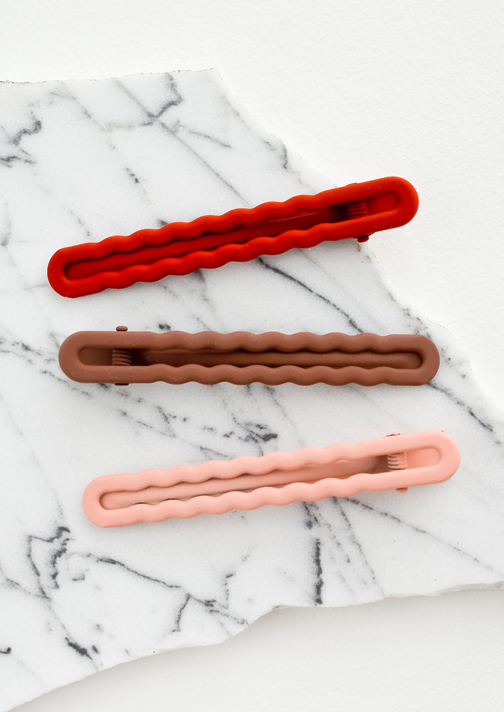 Three hair clips with wavy squiggle design in gradient red hues.