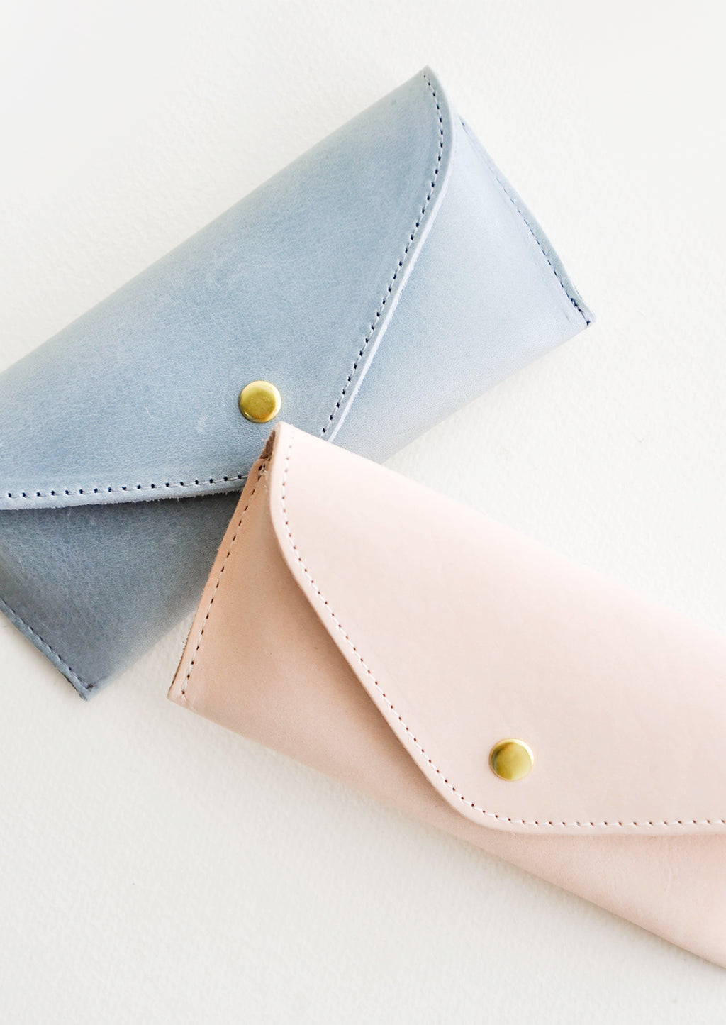 1: Two leather cases for sunglasses that fold close with a snap, one blue and one pink.