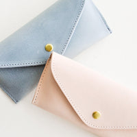 1: Two leather cases for sunglasses that fold close with a snap, one blue and one pink.