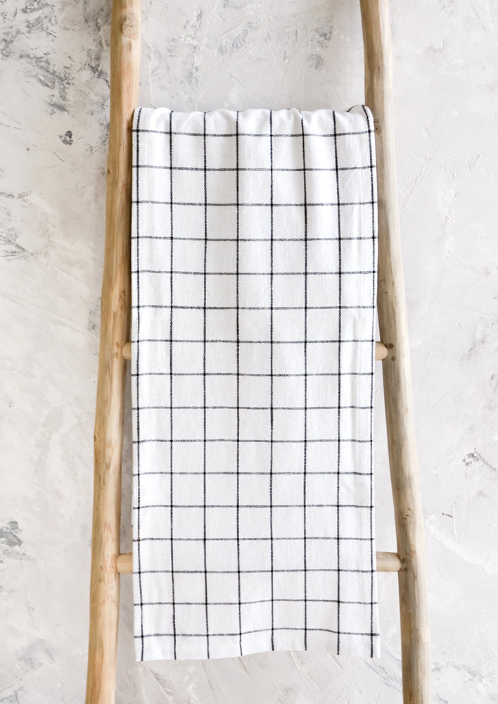 White cotton table runner with black grid check print, hanging on display ladder