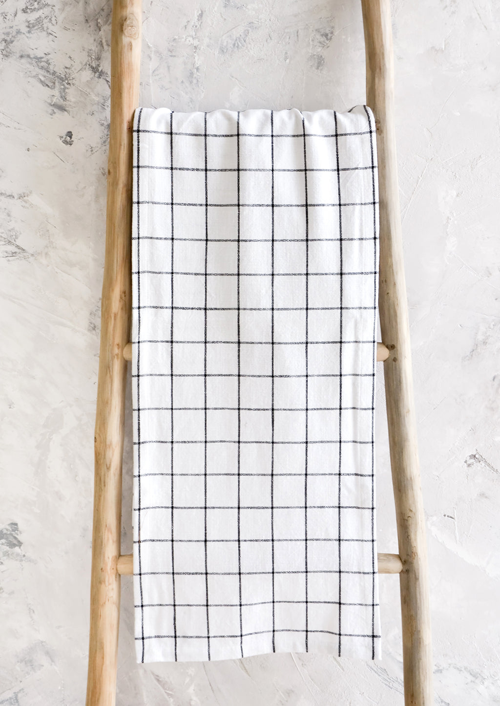 2: White cotton table runner with black grid check print, hanging on display ladder