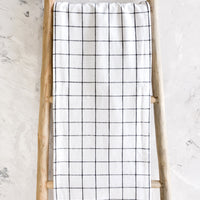 2: White cotton table runner with black grid check print, hanging on display ladder
