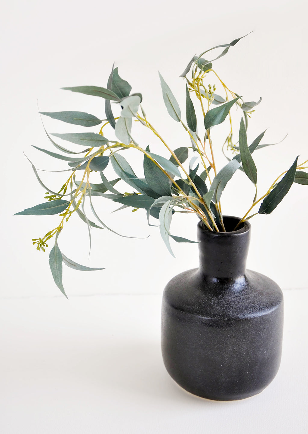 2: Glossy black ceramic vase with wide base and narrow opening, displayed with eucalyptus branch