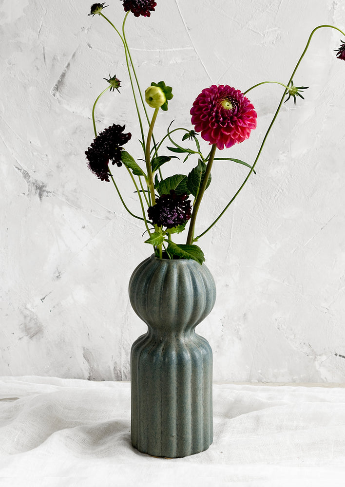 2: A curvy ceramic vase in teal glaze with ball-shaped top, holding flowers.
