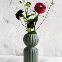 2: A curvy ceramic vase in teal glaze with ball-shaped top, holding flowers.