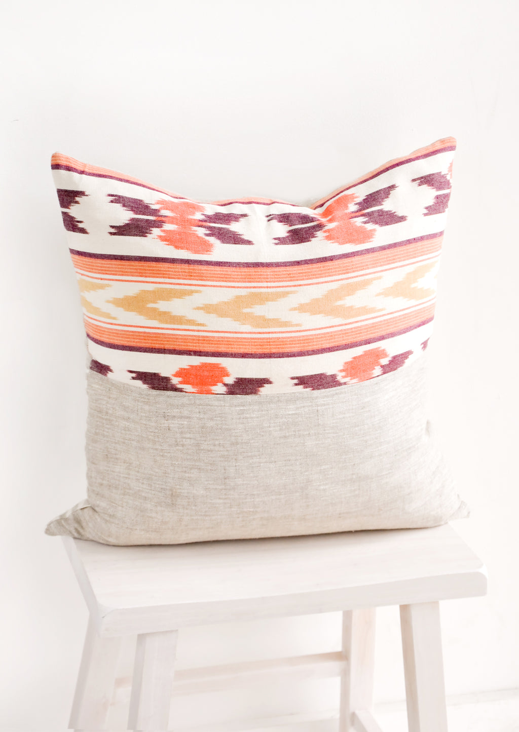 1: Square throw pillow in mixed fabrics. Top half is ikat print in orange and red, bottom half is plain linen.