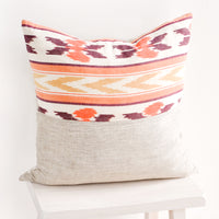 1: Square throw pillow in mixed fabrics. Top half is ikat print in orange and red, bottom half is plain linen.