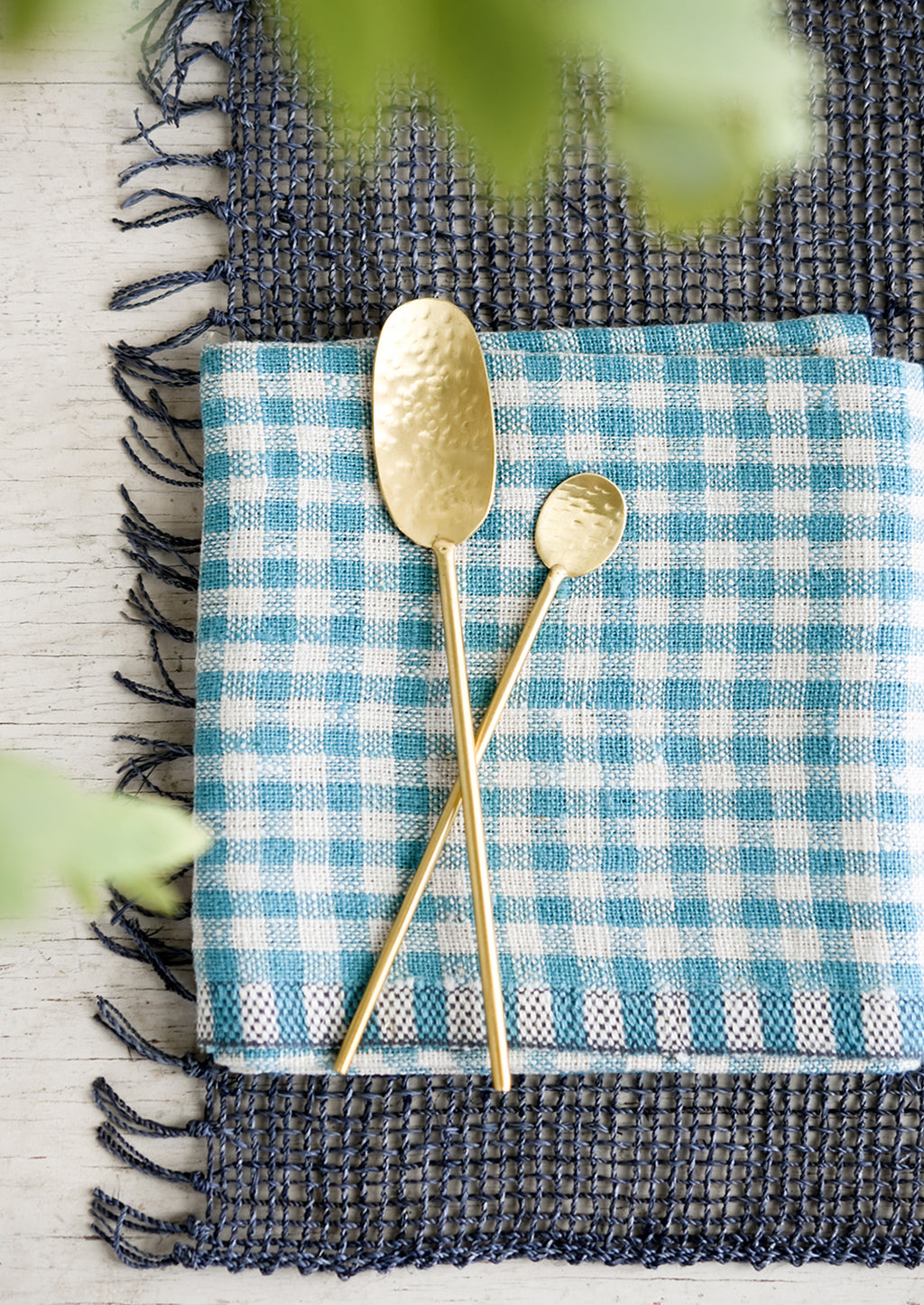 2: Hammered gold spoons on a blue gingham cloth.