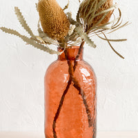 Bing Cherry: A tall glass vase in rosewood hue with hammered texture, displaying dried banksia flowers.