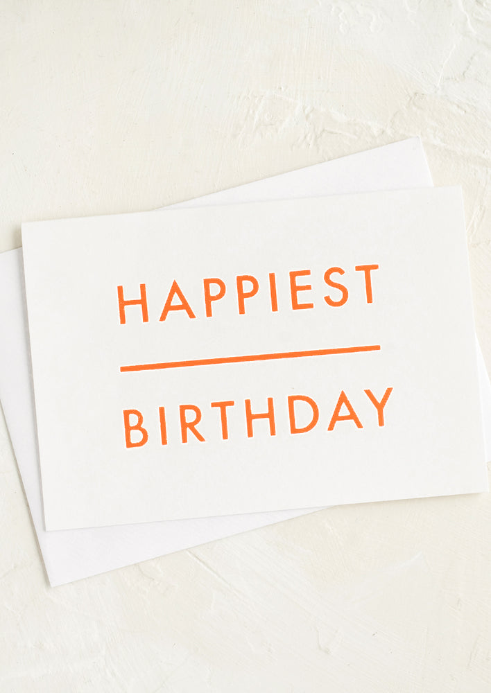 A birthday card with white background and orange text reading "HAPPIEST BIRTHDAY".
