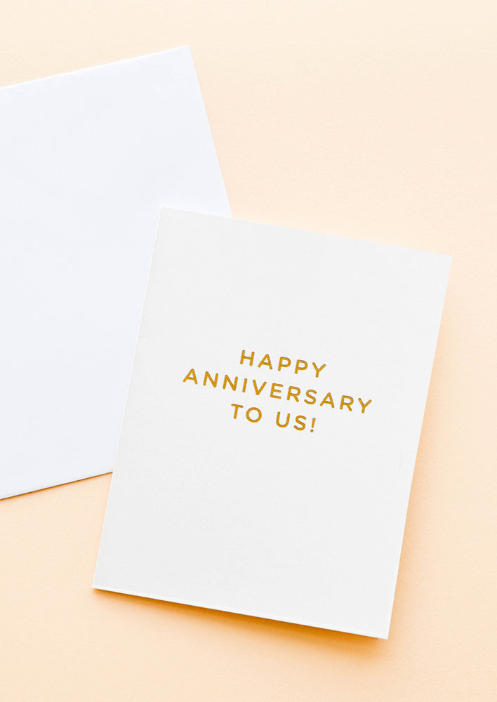 A pale gray greeting card with gold foil text reading "happy anniversary to us."