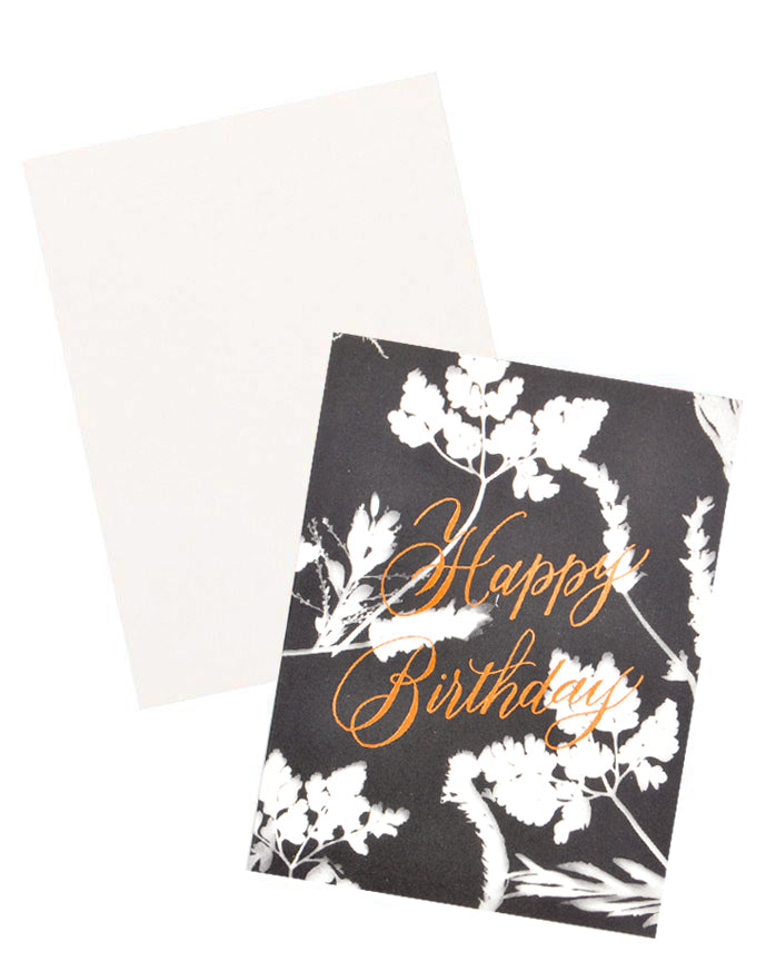 3: Notecard with white flowers on black background and the text 'Happy Birthday" in metallic script, with white envelope.