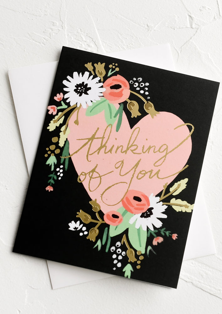 A black greeting card with heart and flowers and text reading "thinking of you".