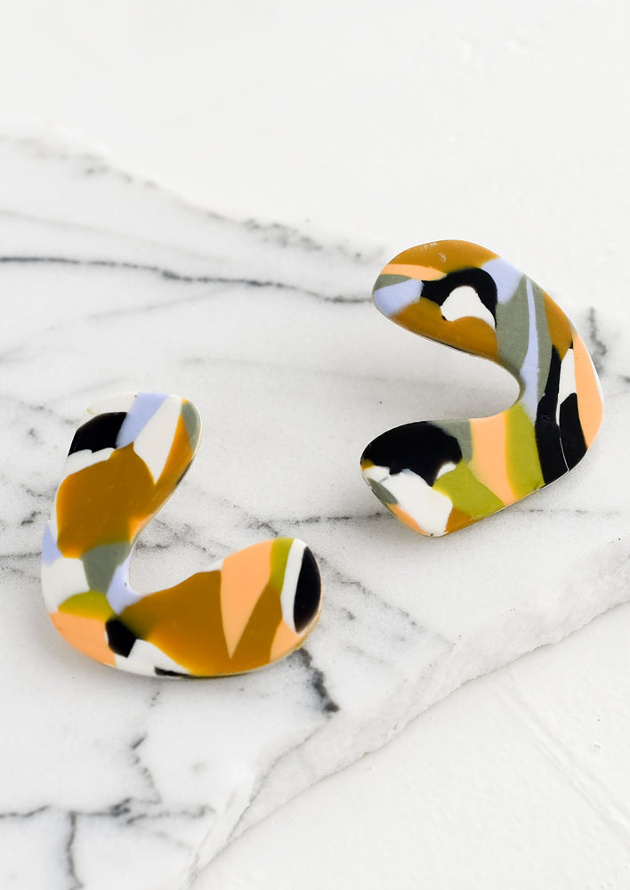A pair of clay earrings in boomerang shape with multicolor marbled pattern.