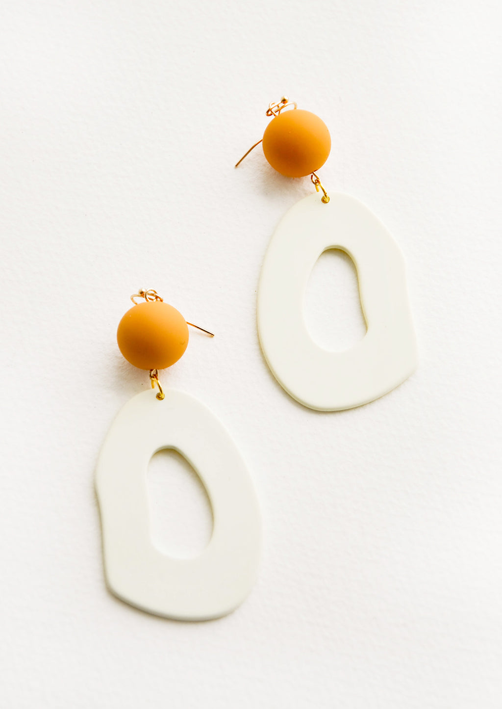 Ivory / Caramel: Dangling earrings featuring asymmetric ivory cut out oval hanging from amber bead.