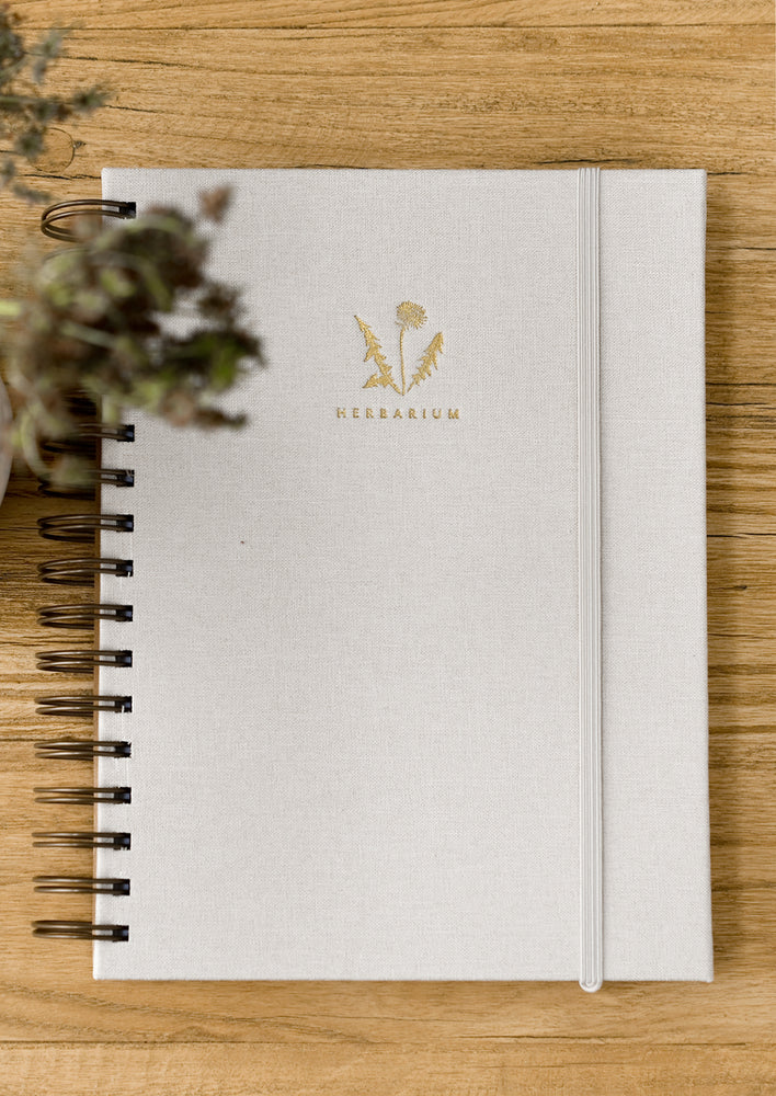 A cloth covered spiral bound journal with gold foil fern and "Herbarium" in small text.