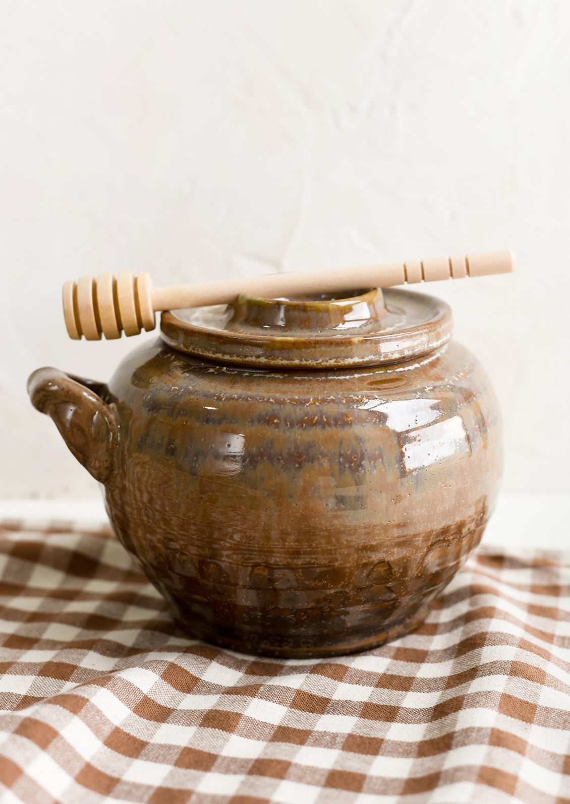 A brown ceramic honey jar with dipper resting on lid.