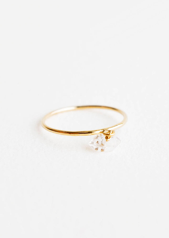 Slim yellow gold ring with a dangling white faceted stone.