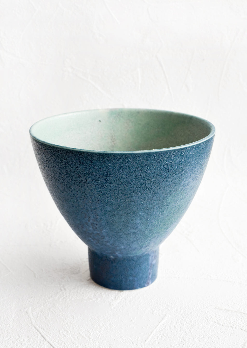 1: Round ceramic planter with tapered, footed silhouette. Textured deep blue glaze with turquoise interior.