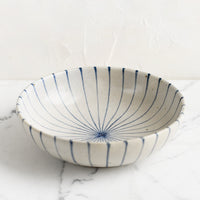 2: A round and shallow bowl in white with blue sunray pinstripe pattern.