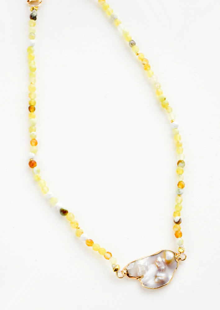 Beaded necklace with round gemstone beads in variegated lemon yellow, asymmetrically shaped grey pearl pendant at front and center