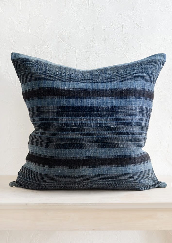A square throw pillow in indigo fabric with variegated black stripes.