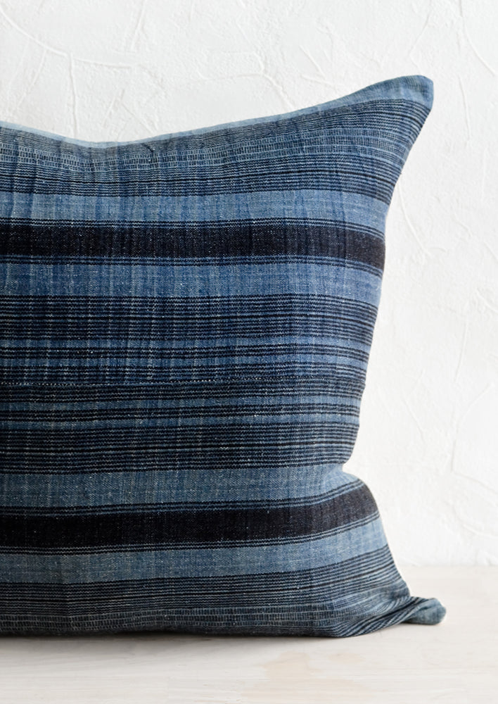 A throw pillow in indigo fabric with variegated black stripes.