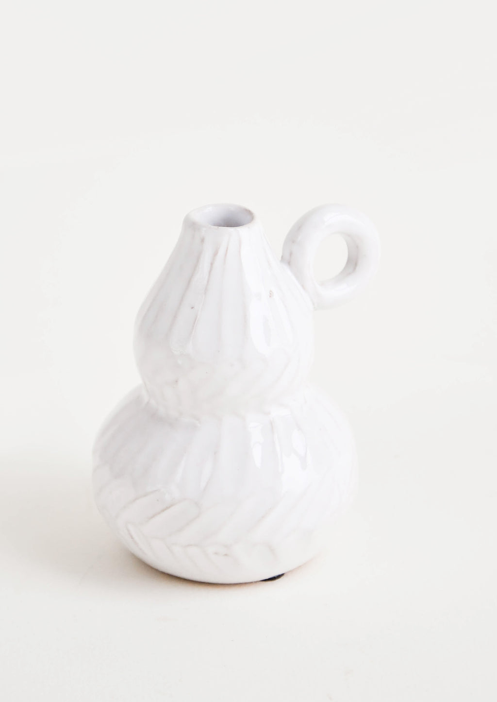 1: White ceramic bud vase with pinched center and tapered top. Small, round handle at side. Allover etched texture.