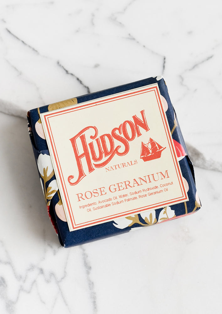 A square bar of soap in botanical printed packaging in Rose Geranium scent.