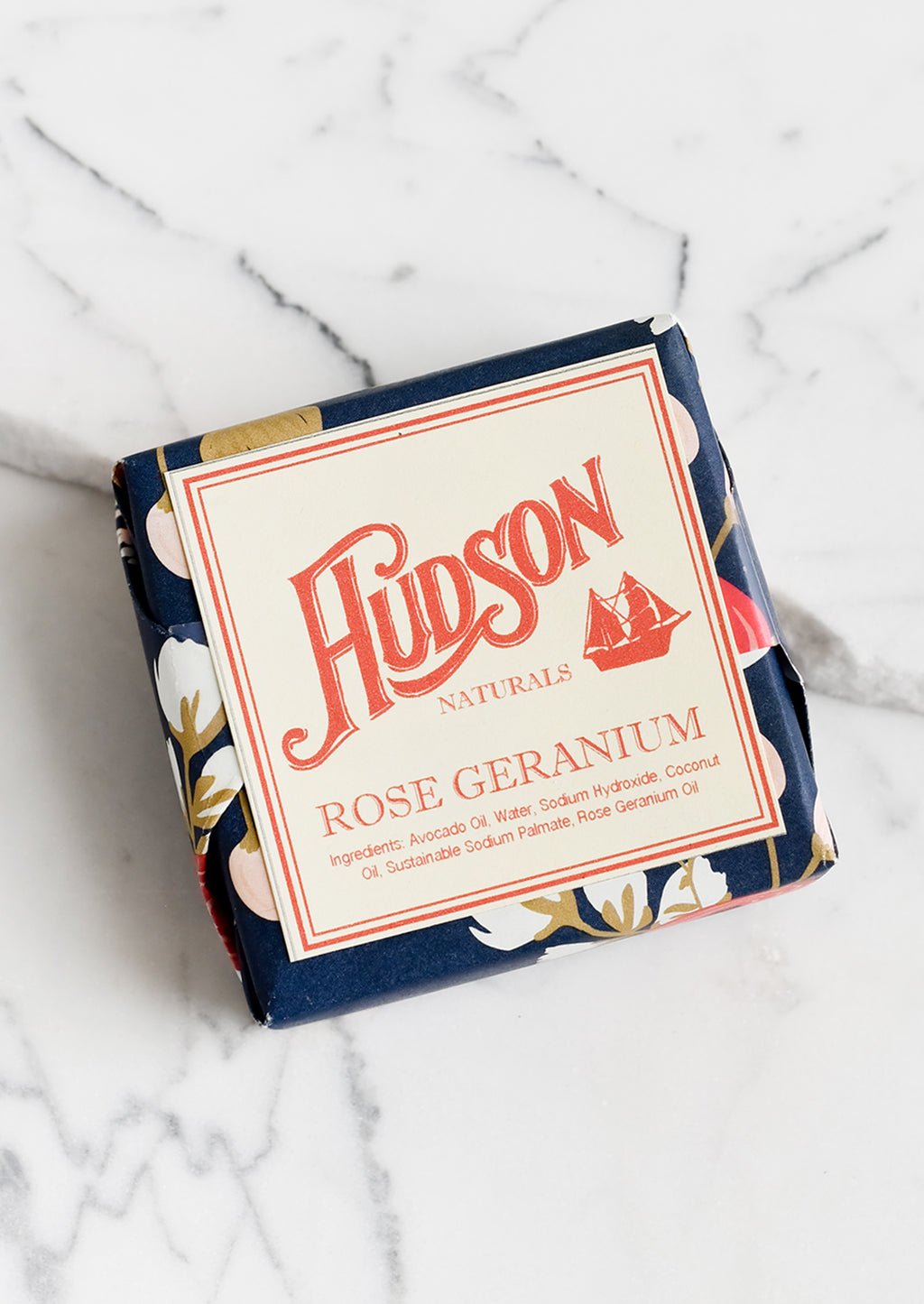 Rose Geranium: A square bar of soap in botanical printed packaging in Rose Geranium scent.