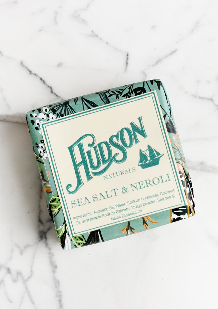 A square bar of soap in botanical printed packaging in Sea Salt & Neroli scent.