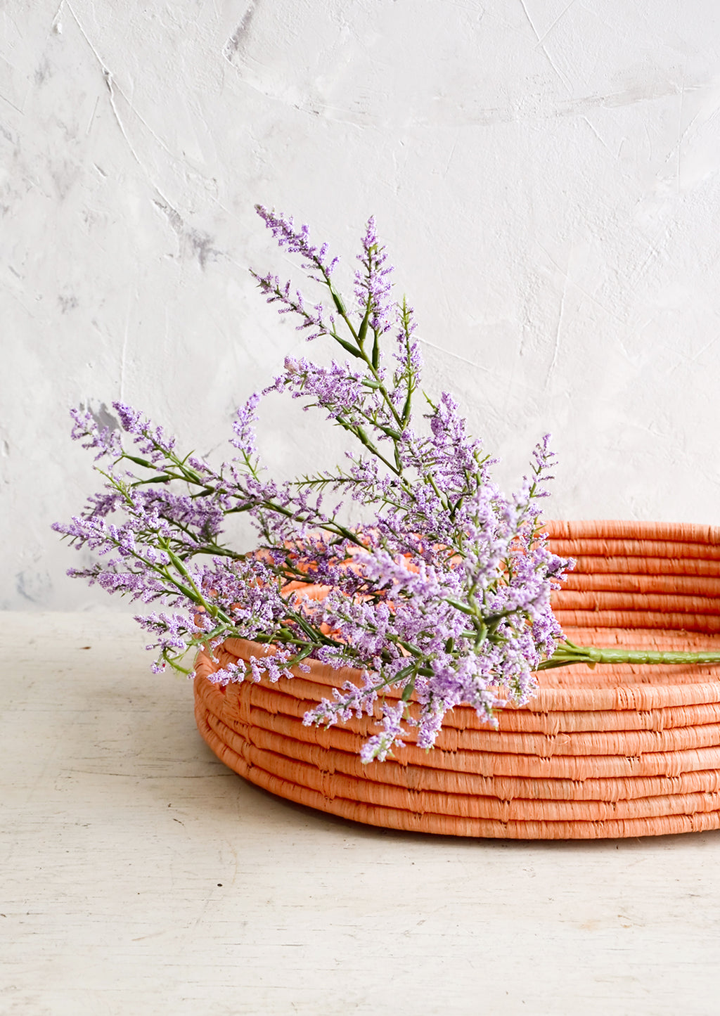 2: Woven raffia basket in peach color, housing purple flowers.