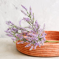 2: Woven raffia basket in peach color, housing purple flowers.