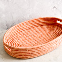 1: Oval shaped, shallow basket woven in peach raffia with cutout handles at sides.