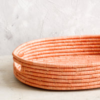 4: Oval shaped, shallow basket woven in peach raffia with cutout handles at sides.