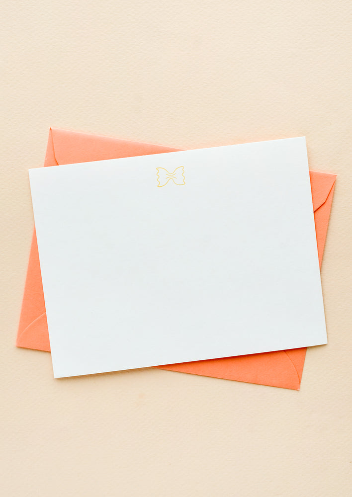 A coral colored envelope with white notecard and small icon of a piece of bowtie pasta printed at top.