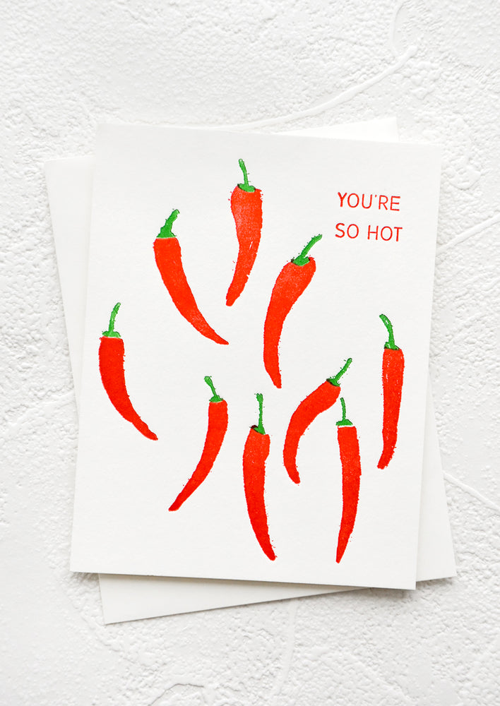White greeting card with multiple red peppers on front and text at corner reads "You're so hot"