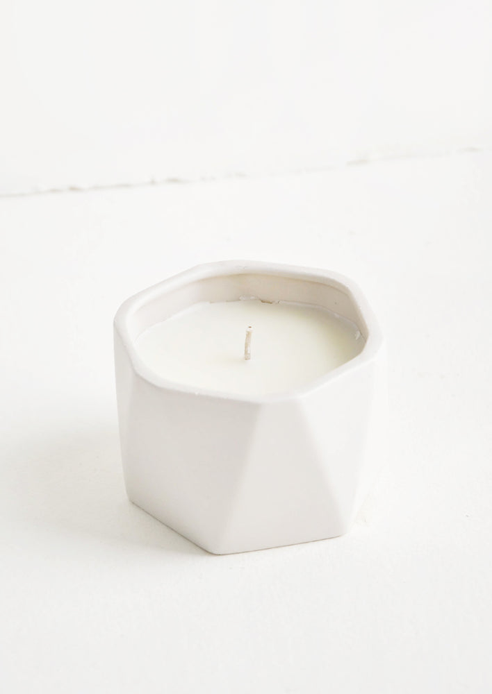 A small candle in white faceted ceramic vessel.