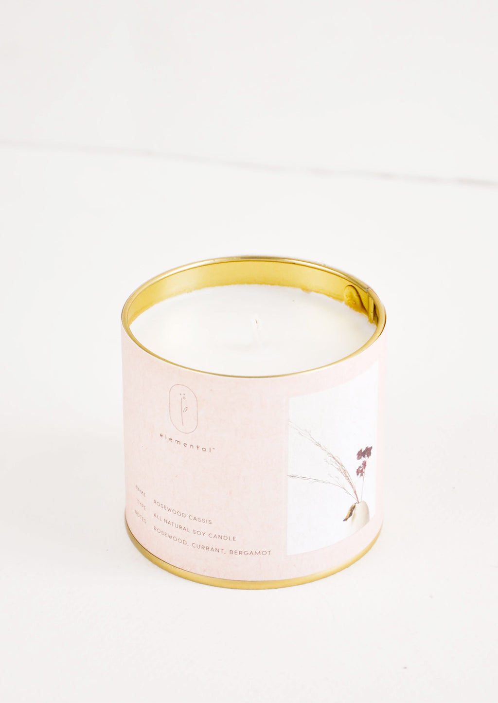 Rosewood Cassis: A candle in a brass tine with a pale pink label featuring a picture of a flower.
