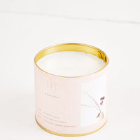 Rosewood Cassis: A candle in a brass tine with a pale pink label featuring a picture of a flower.