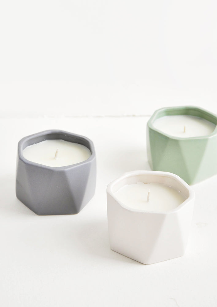 1: Three small candles in faceted ceramic vessels in assorted colors.