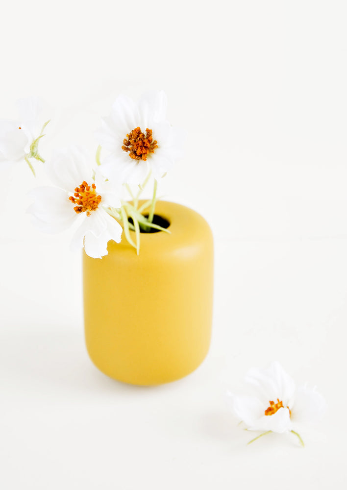 Small, tubular shape ceramic bud vase in matte mustard, shown with flowers