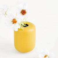 2: Small, tubular shape ceramic bud vase in matte mustard, shown with flowers